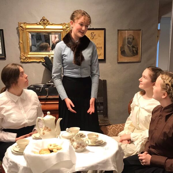 Fire jenter rundt et bord. Tre sitter og ei står. Foto