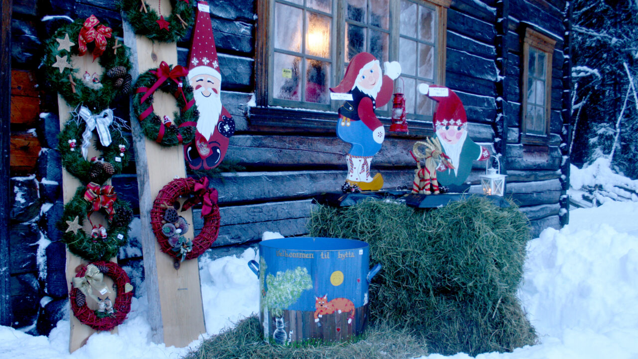 Julepynt og nisser utenfor et gammelt tømmerhus. Foto