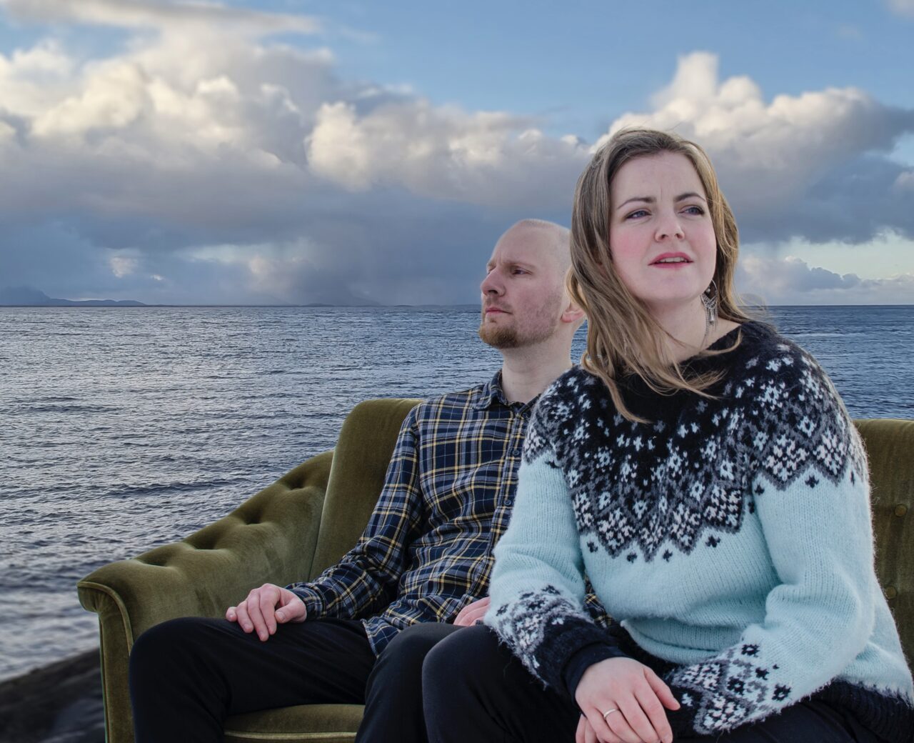 En mann og en dame sitter i en grønn sofa ved havet