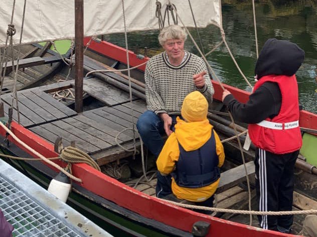 En mann og to barn i en liten båt ved brygga