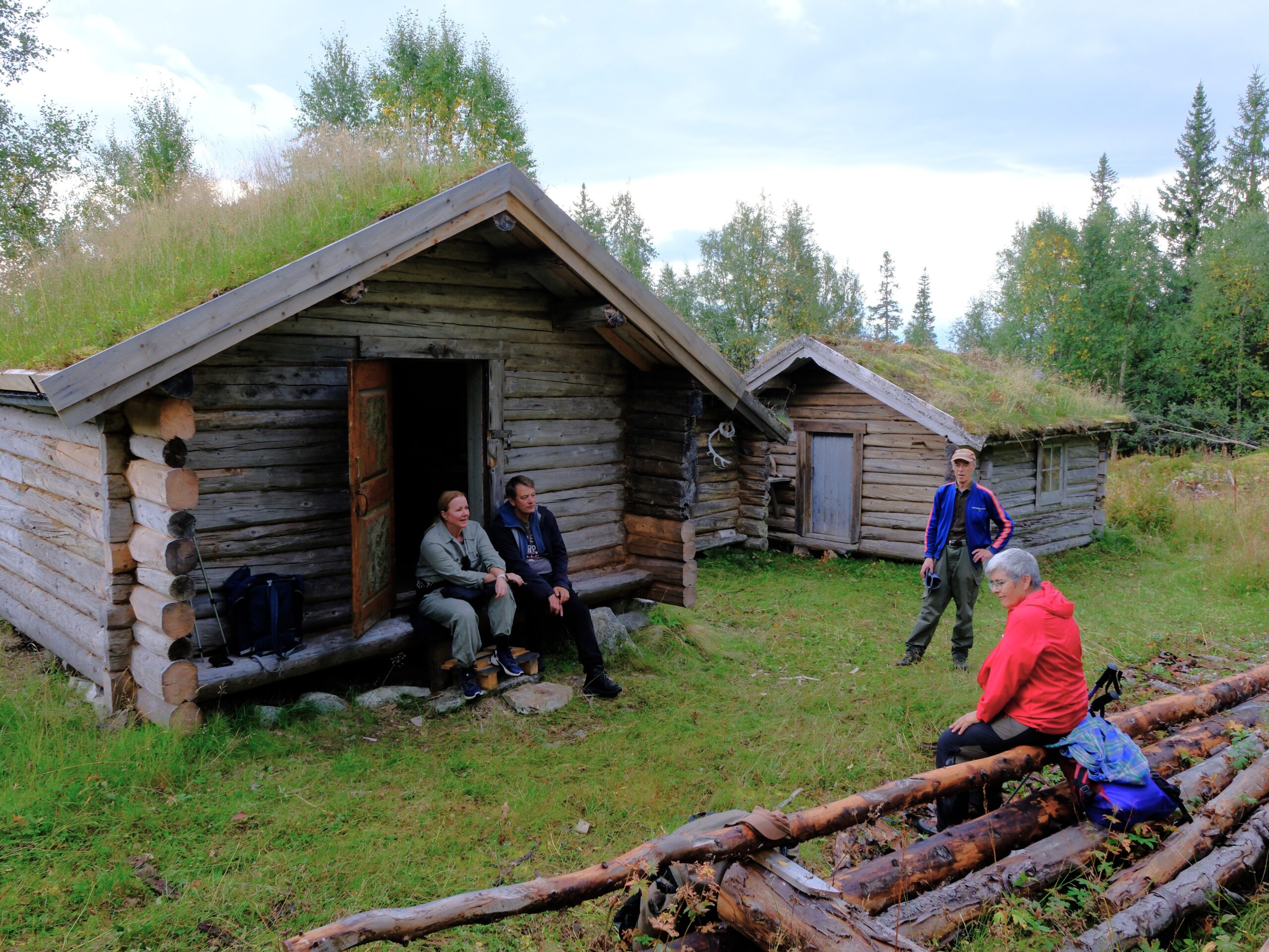 To laftede bygg på Lisetra. I det ene sitter to mennesker i inngangspartiet, en står på gresset bortenfor den andre bygget og en dame i rød jakke sitter på en skigard(gjerde)