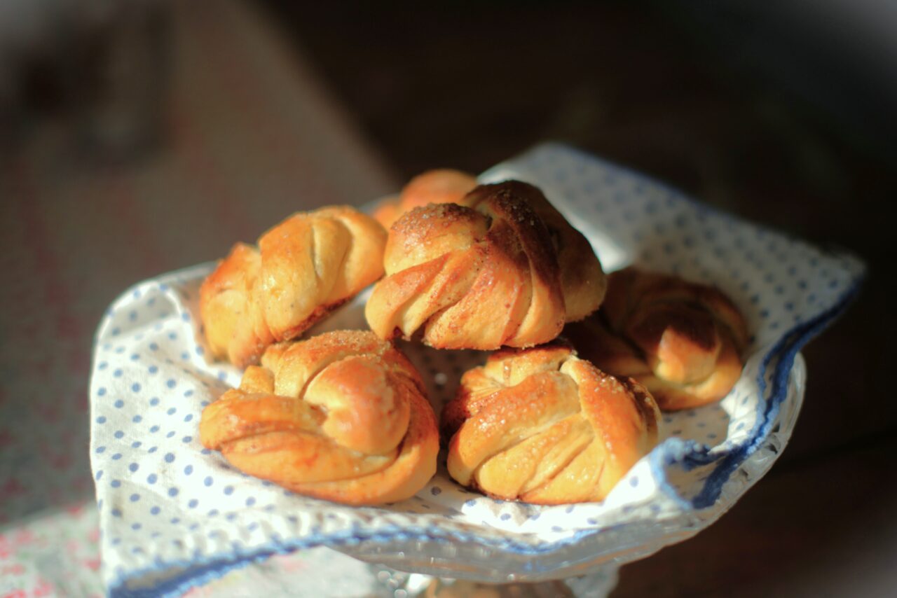 kanelsnurr. allerken med seks gyllenbrune bakverk med tvistet form på hvit duk med blå prikker.