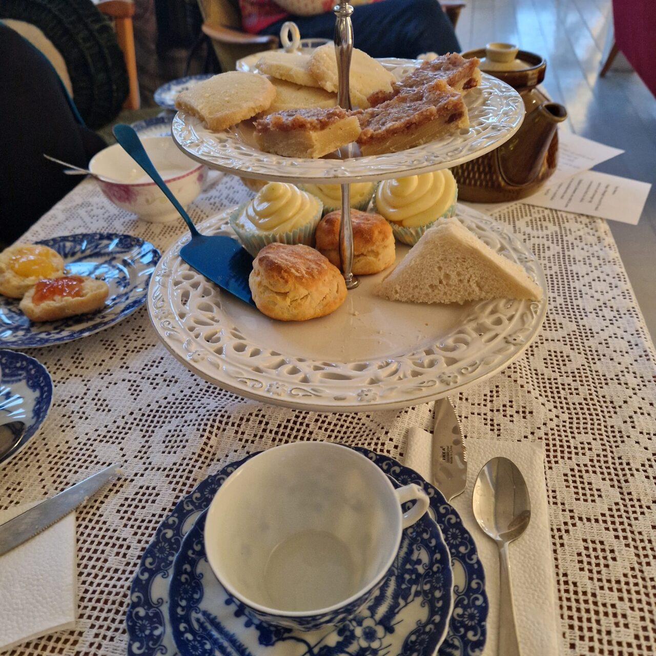 Bord dekket til te med etasjefat med kaker, scones og sandwicher, samt tekanne og servise.