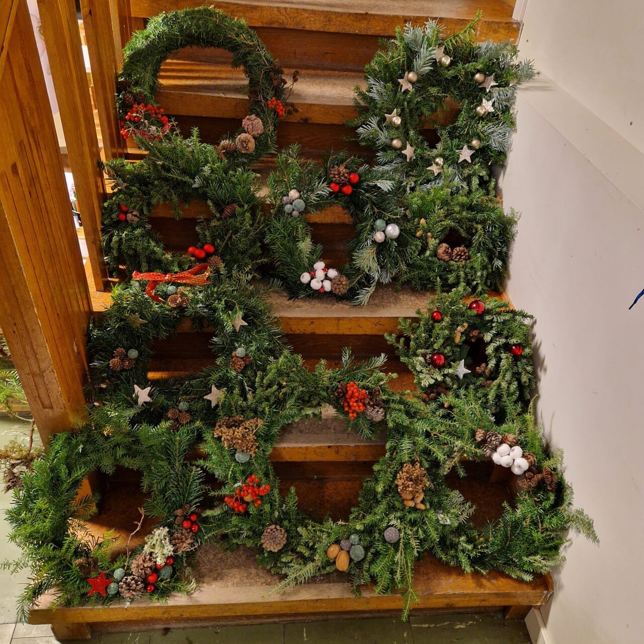 Tretrapp dekorert med julekranser med grønt løv, kongler, røde bær og hvite stjerner