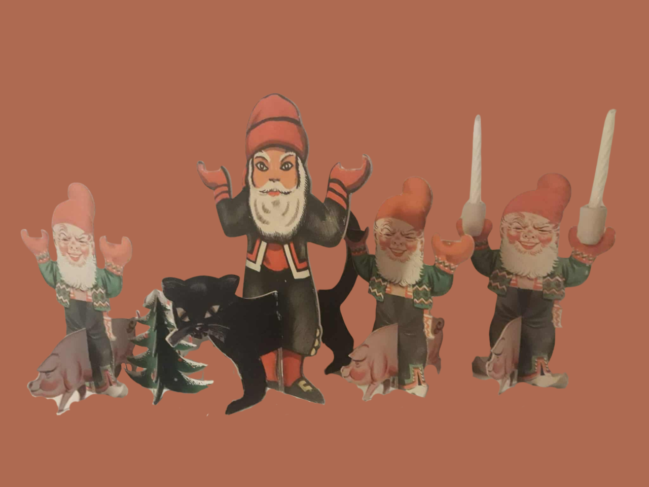 Julekort. Papirfigurer med tre nisser, en større figur i svart, en svart katt, to griser og et lite grønt tre.