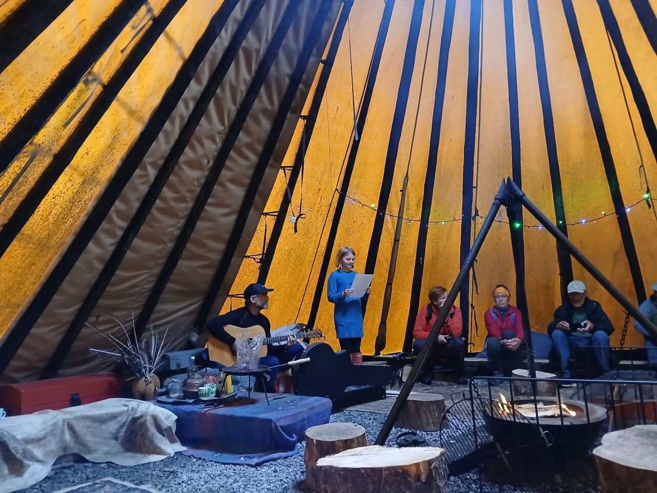 innsiden av en lavvo med flere personer samlet rundt et ildsted.