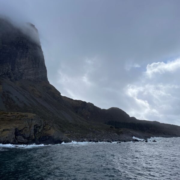 Et bilde av en klippe/fjellformasjon ved havet under en overskyet himmel.